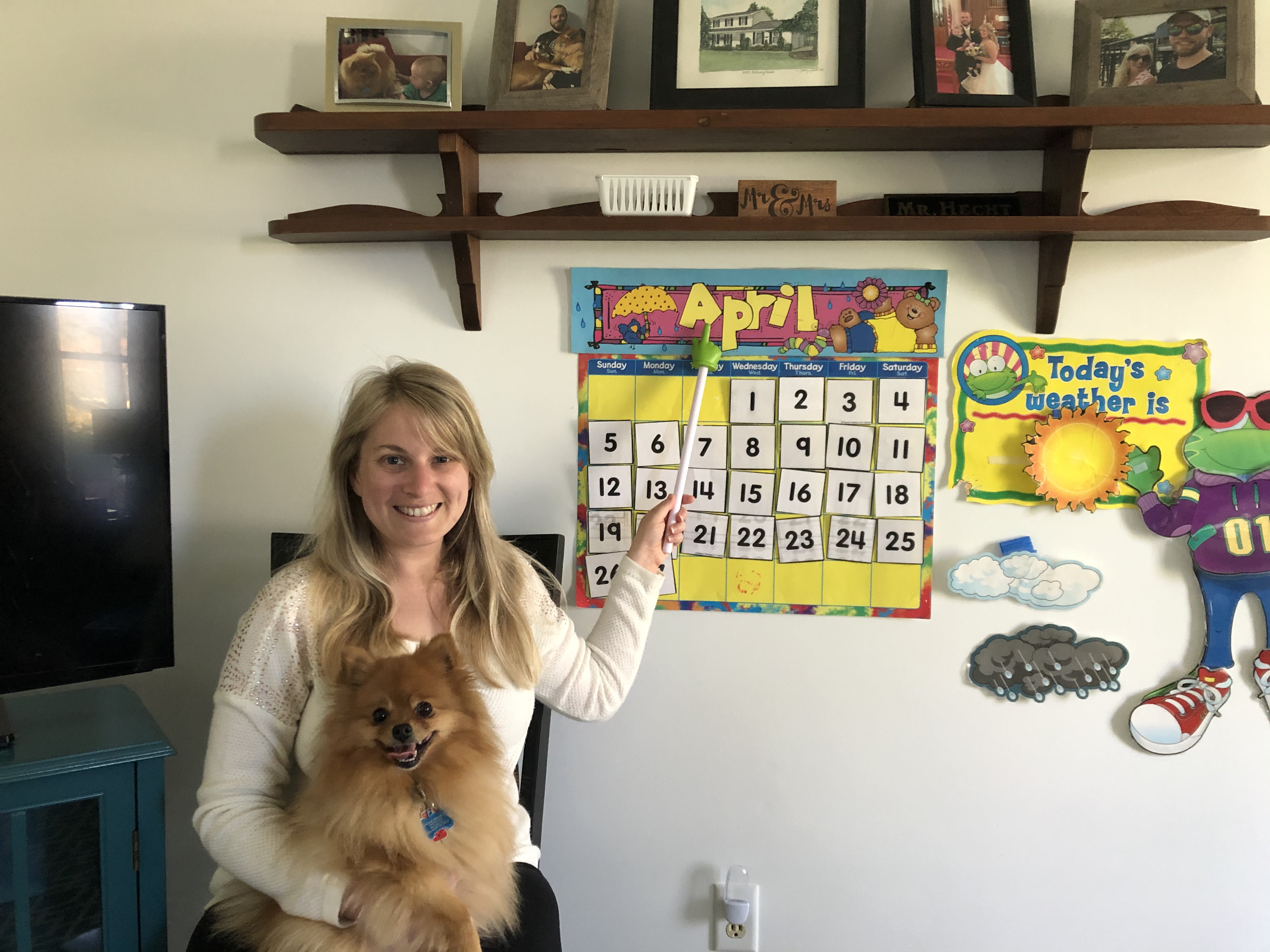 A blonde woman pointing to a child's calendar. She has a gold Pomeranian in her lap.