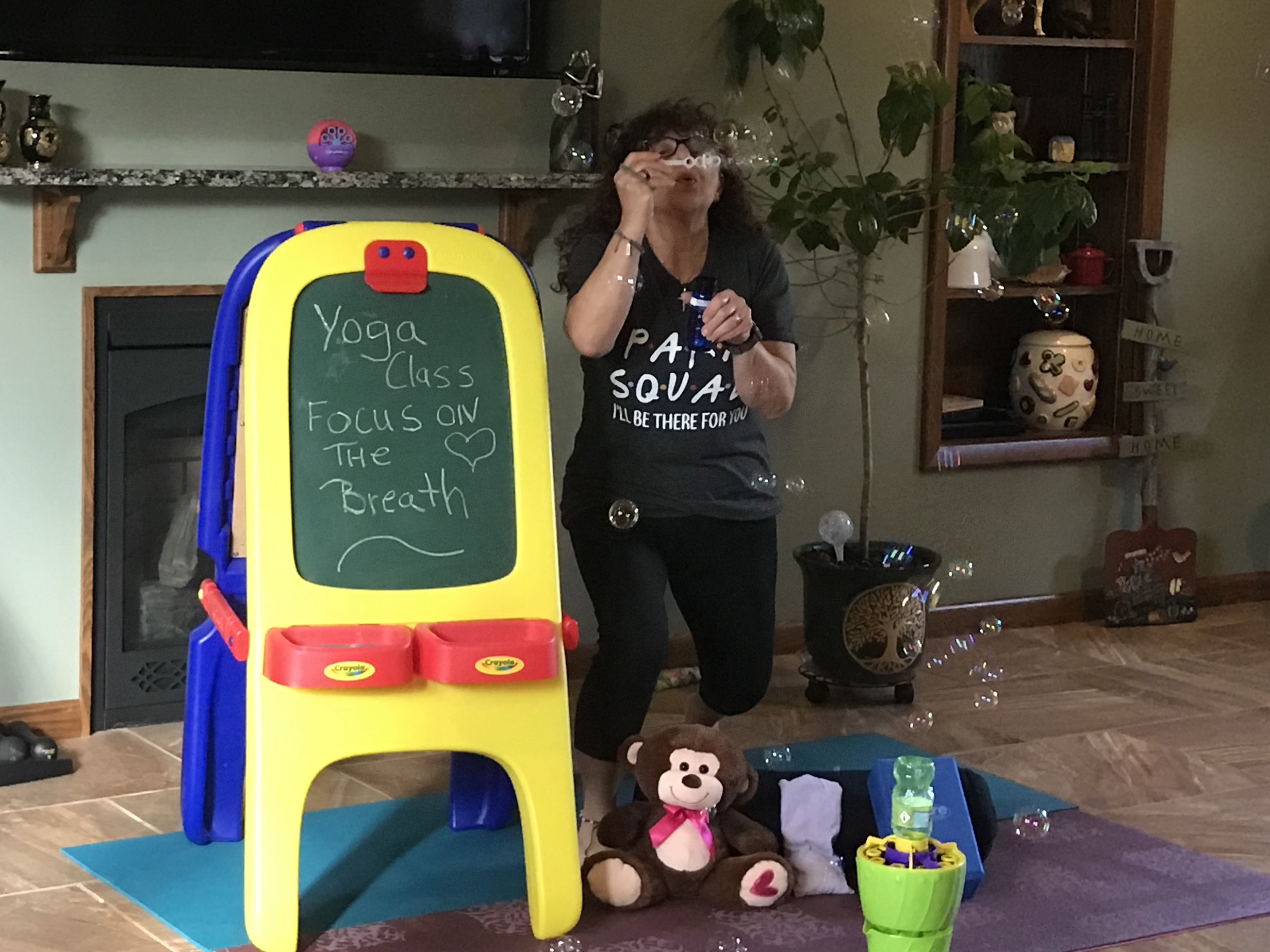 A dark-haired woman standing by a child's chalkboard, blowing bubbles