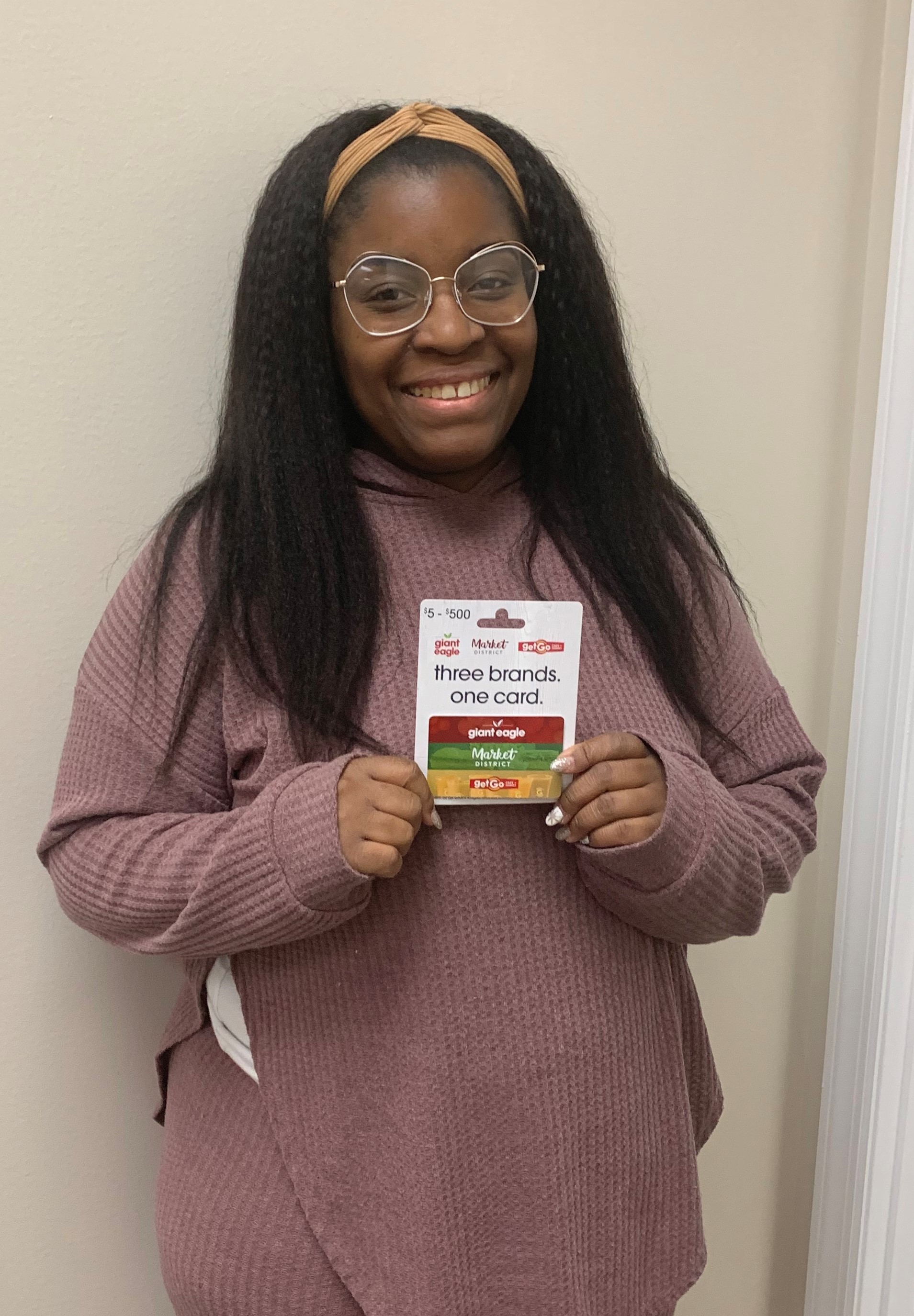 A black woman with glasses and a headband, holding a gift card