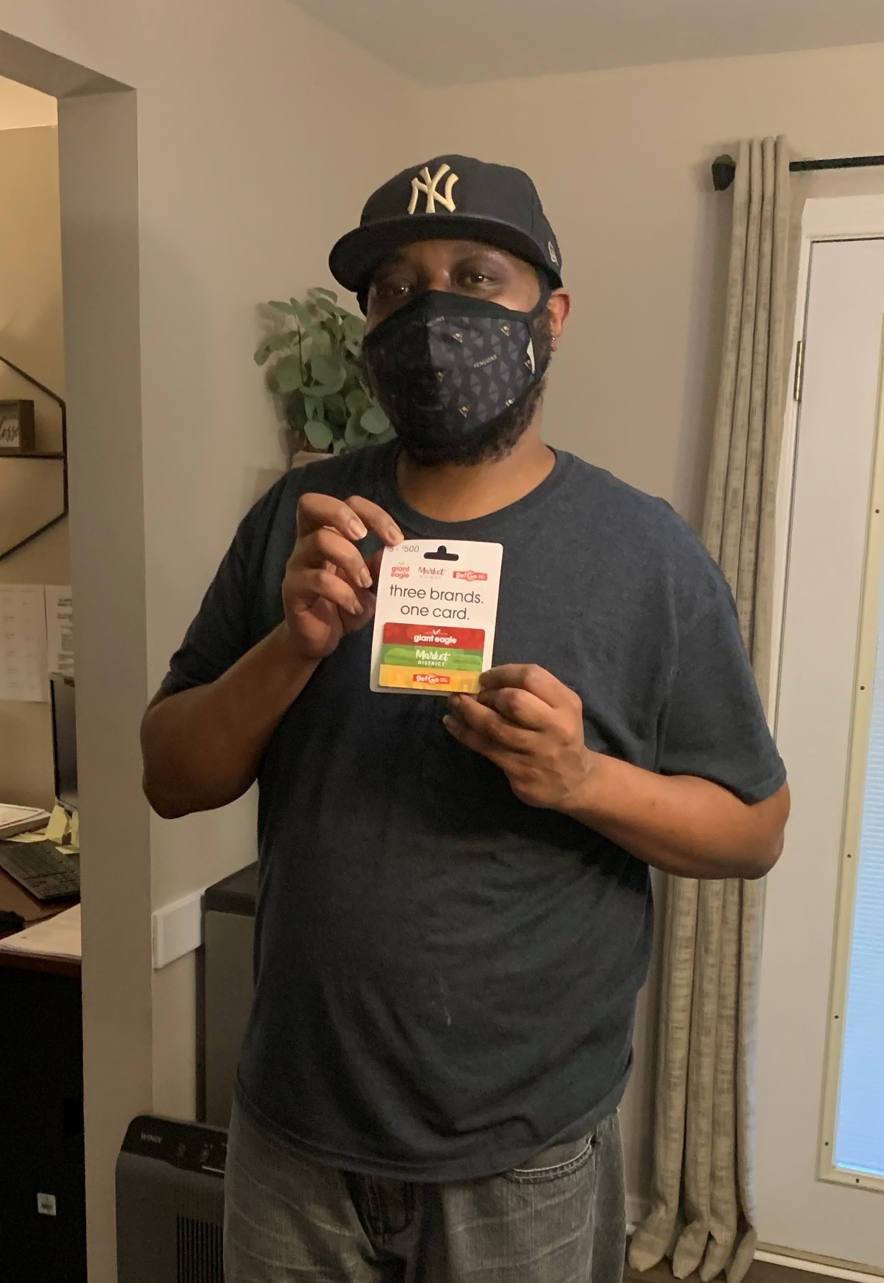 A black man in a mask and hat, holding a gift card