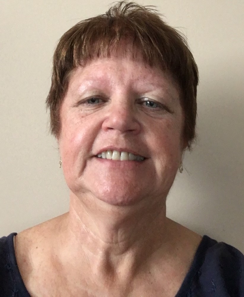 An older woman with very short brown hair smiling at the camera