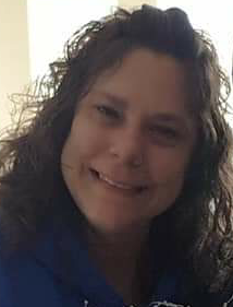 A woman with long, curly brown hair smiling at the camera